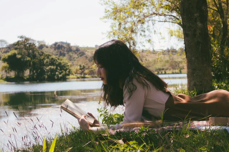 a woman reads a book in the park by the lake