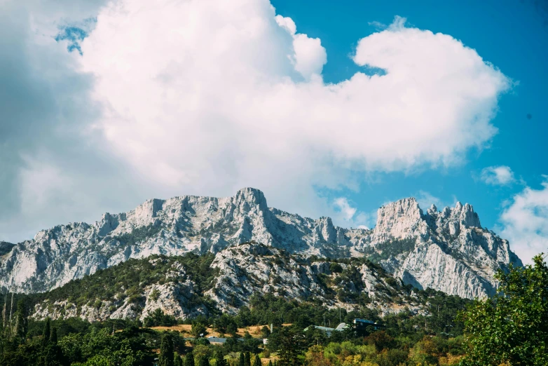 mountains rise above the forest under a cloudy blue sky