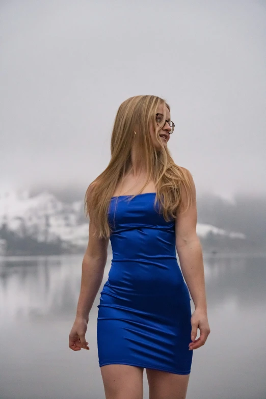 a woman standing on the side of a lake, with her dress rolled over