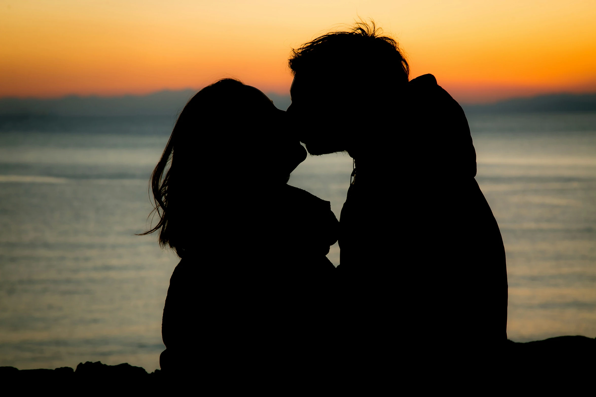 silhouette pograph of a kissing couple with the sun setting in the background