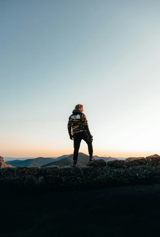 a man with a jacket and jeans stands on a rock near the water