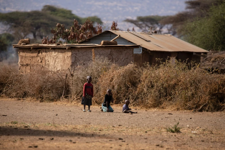 a couple of children playing outside of a hut