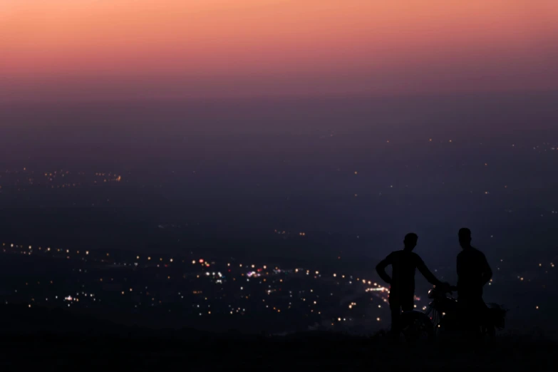 the two people are standing on top of the hill overlooking the town