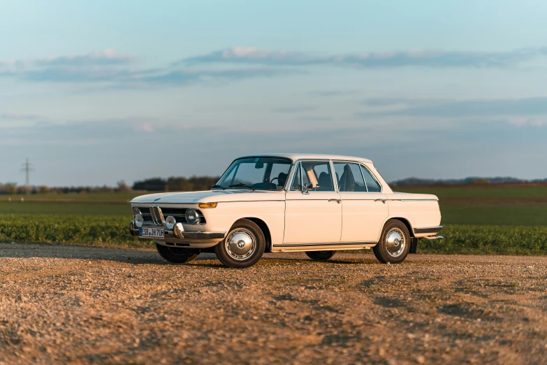 an older car sits parked on the dirt road