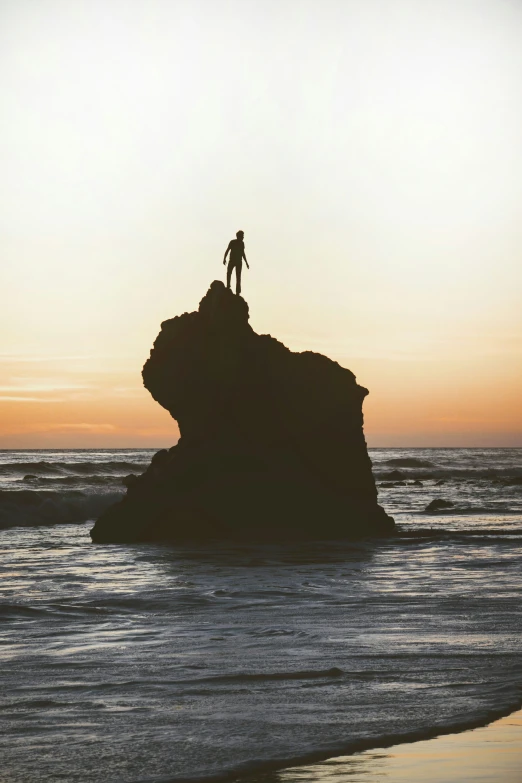 a man standing on top of a rock at the beach