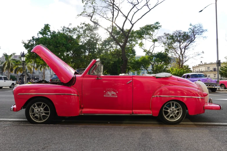 a red classic car on the street with a large hood open