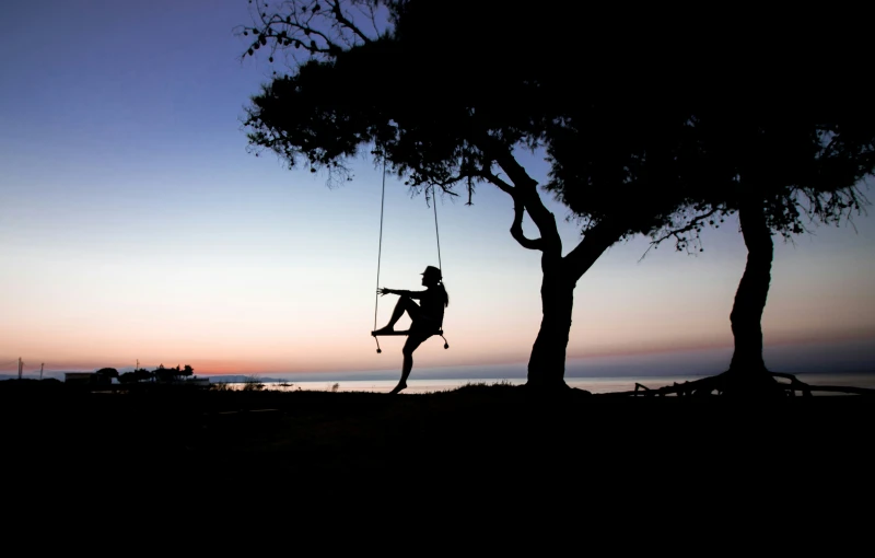 man in black shirt on rope swing while holding on to tree
