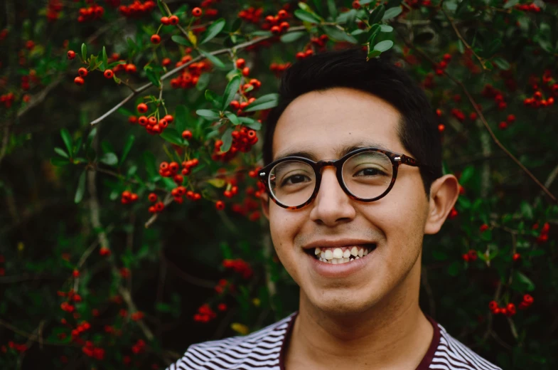 a man in glasses smiles with berry bushes behind him