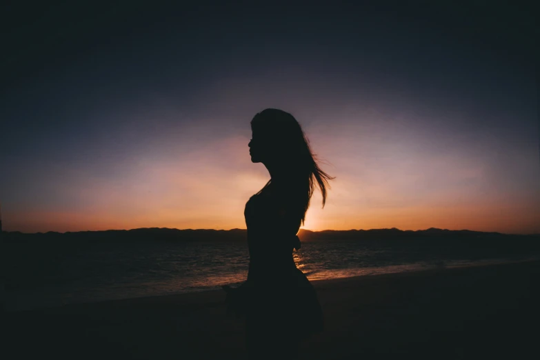 a woman standing on a beach at sunset