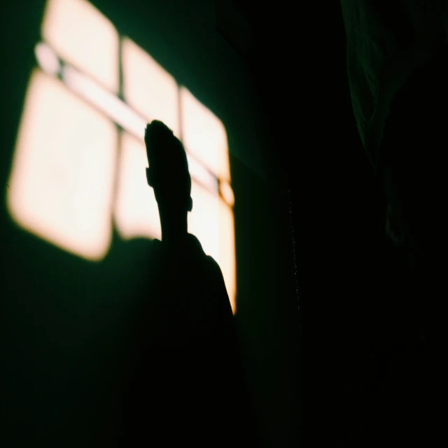 a man standing in the dark under a shadow from an open window