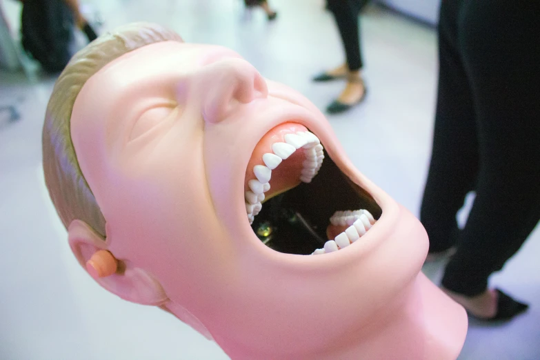 an open mouth of a plastic doll standing next to other people