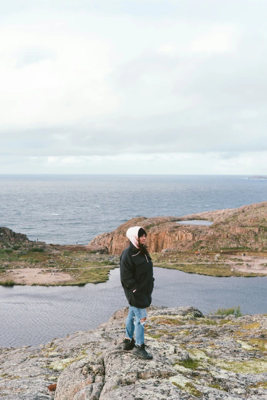 the person is standing on a rocky ledge near the water