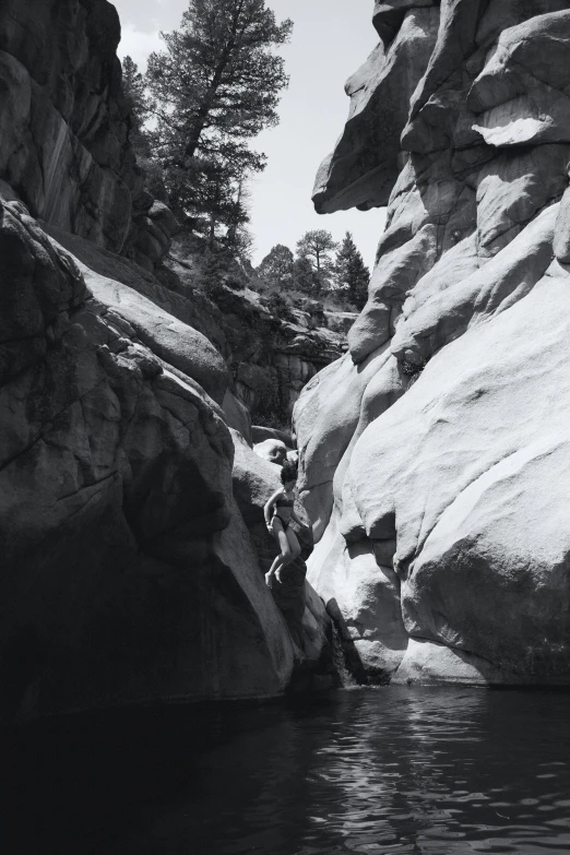 black and white image of people in water next to a large rock