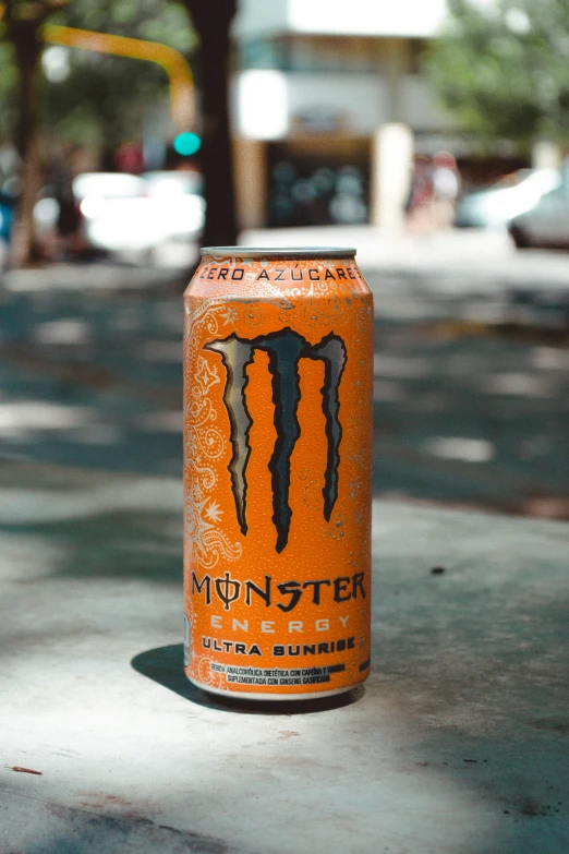 an orange can of monster energy drink sitting on the ground