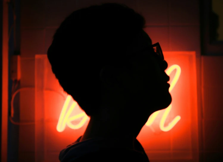 a person wearing dark glasses standing next to a neon sign