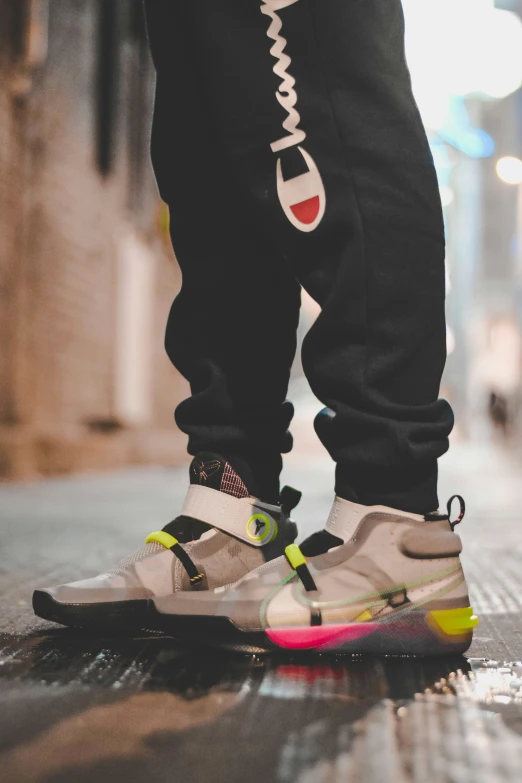 someone standing on the floor in black pants and a pair of pink and yellow sneakers