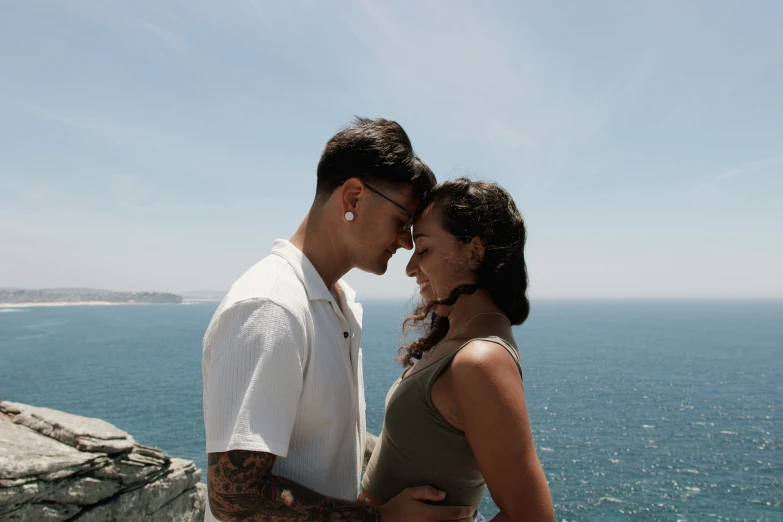 two people stand close together near the ocean