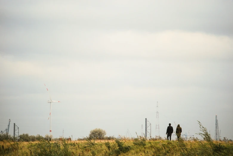 two people standing near a field, observing two windmills