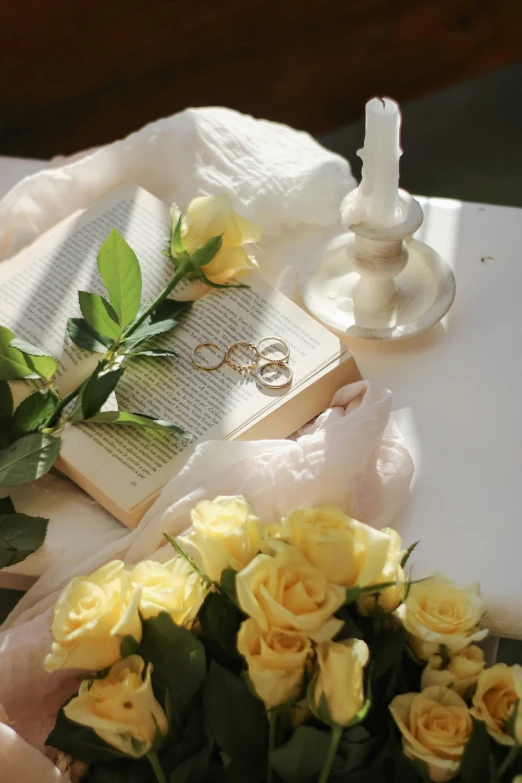 an arrangement of yellow roses on a table beside the book and the candle