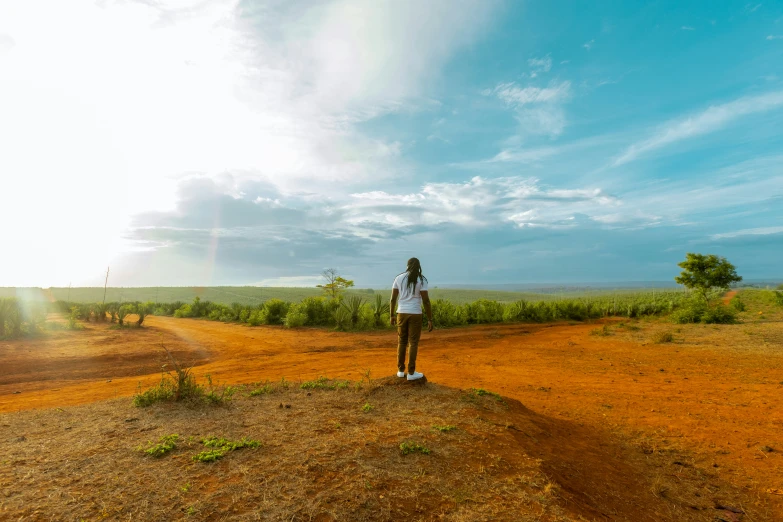 a woman standing on a dirt road surrounded by an empty field