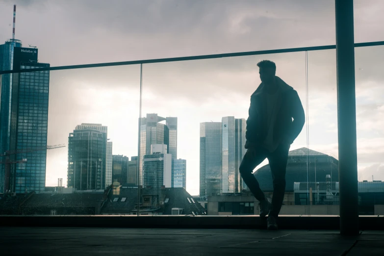 a man stands on the edge of a bridge, against the backdrop of high rise buildings