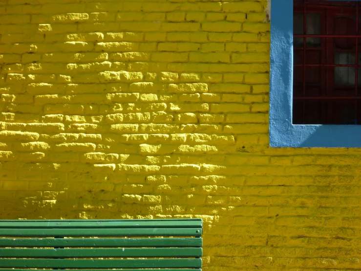 an empty green bench sitting in front of a wall