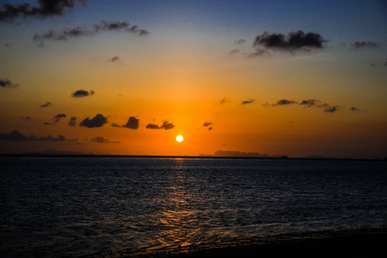 a yellow sun setting over water with some clouds