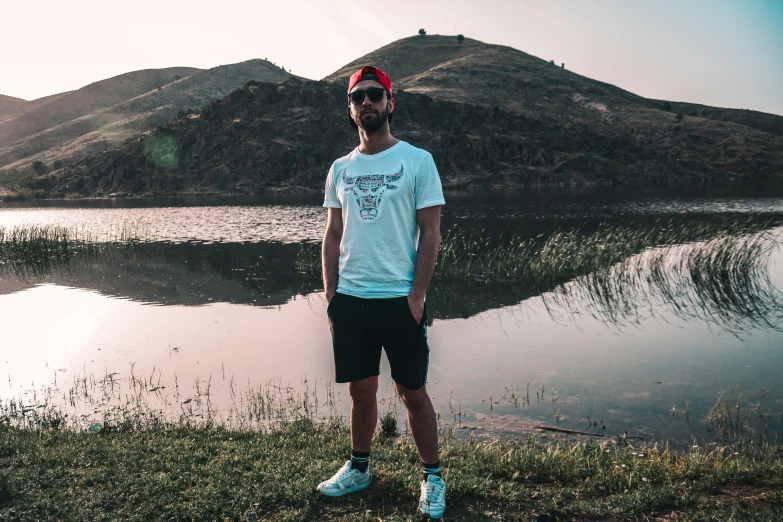 a man standing in front of a lake wearing sunglasses