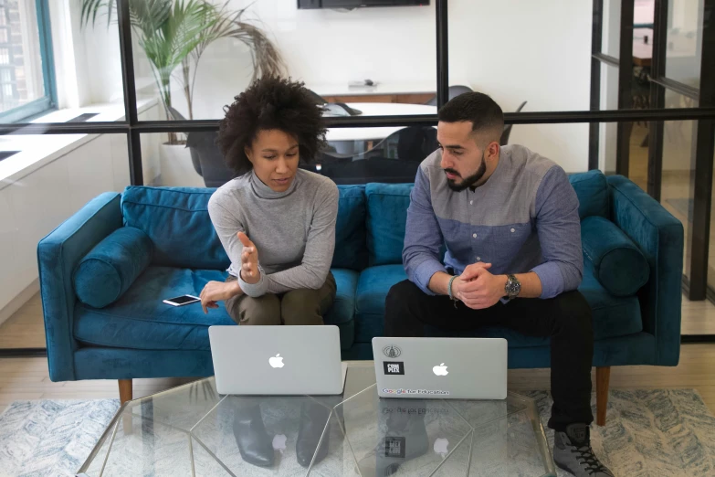 two people sit on a couch with their computers