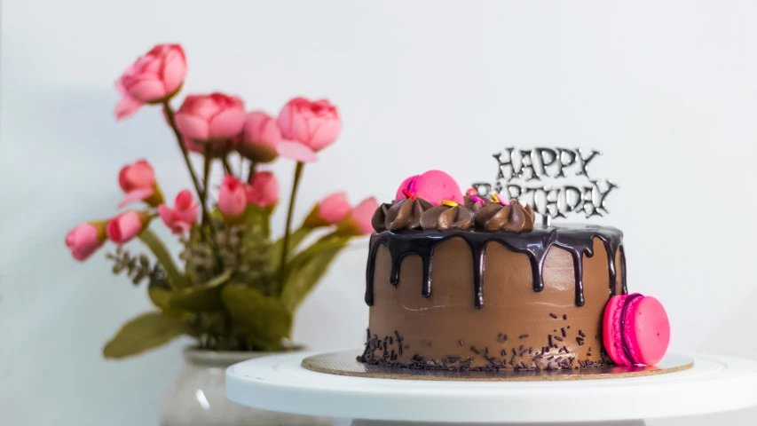 a chocolate birthday cake with pink flowers and a happy birthday cake