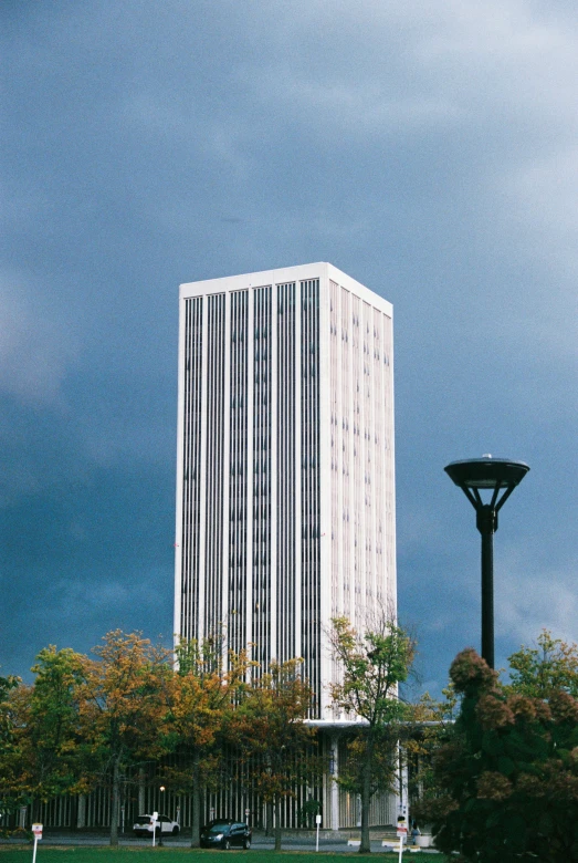 an empty park has some plants on it, while a tall building stands alone against the background of a blue sky