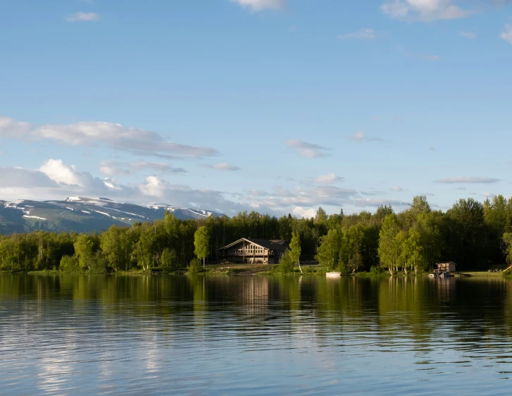 a tree lined lake and mountains in the background