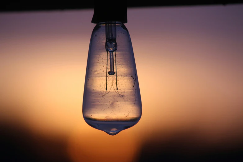 a light bulb hanging upside down in front of a sunset