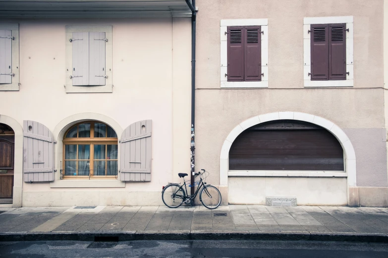 a bike is parked outside of a pink building with shutters