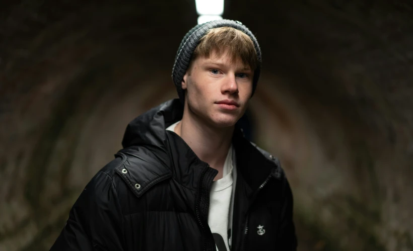 young man wearing coat in a tunnel posing for the camera
