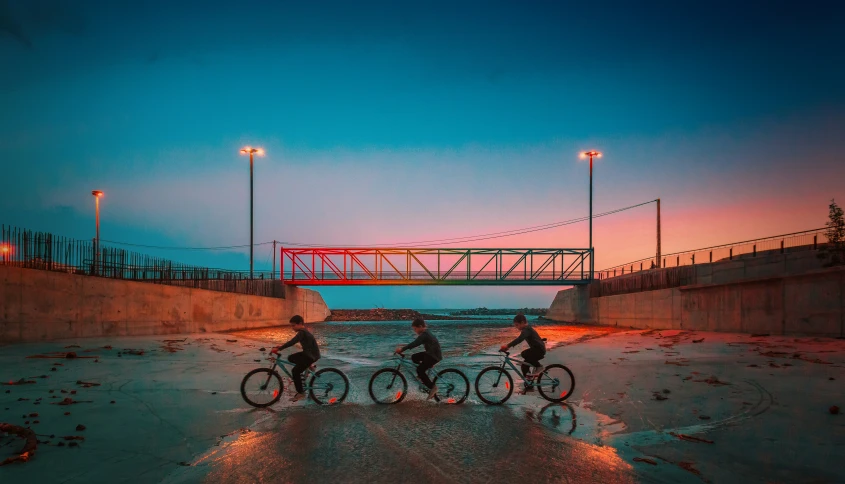 three people riding bikes at dusk next to a bridge