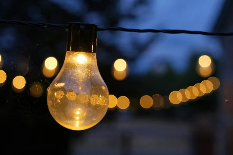 a glowing light bulb suspended on a line with some lights in the background