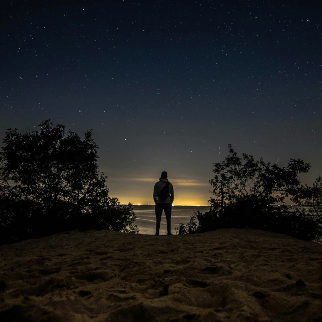 silhouetted man standing at the edge of the water looking up at the sky