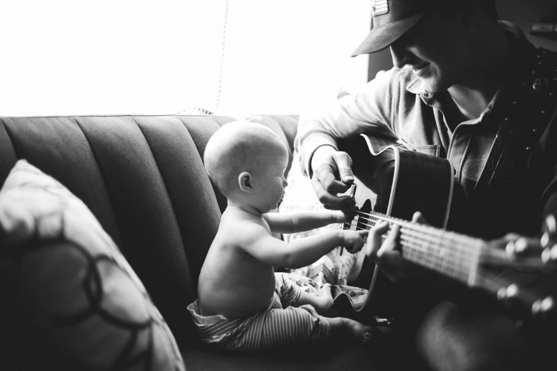 a baby plays an acoustic guitar while sitting next to an older man