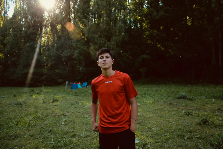 a young man wearing a red shirt posing in front of the sun