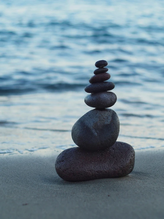 four stacked rocks sit on the beach in the sand