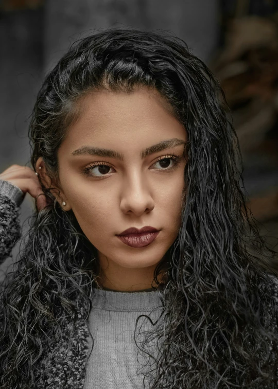 a woman with long black hair, wearing a gray sweater and earrings