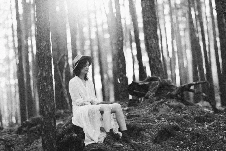 woman in dress and hat sitting on rock in woods