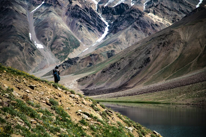 three men walking up a mountain slope with lake in the foreground