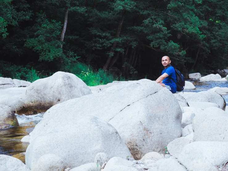 the young man sits on rocks beside the river