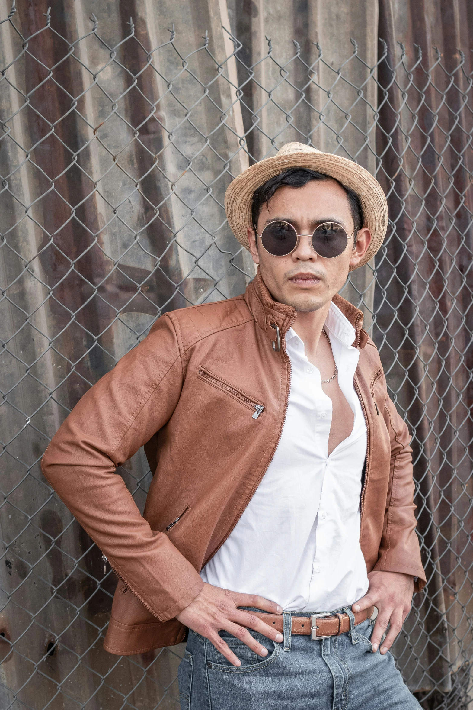 a man posing in front of a fence wearing sunglasses and a jacket