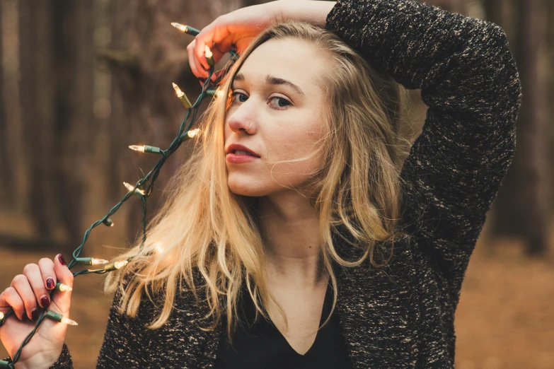 a woman stands in a forest holding a bunch of christmas lights