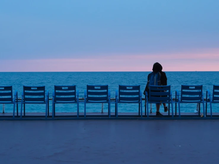 two people sitting on empty chairs near an ocean