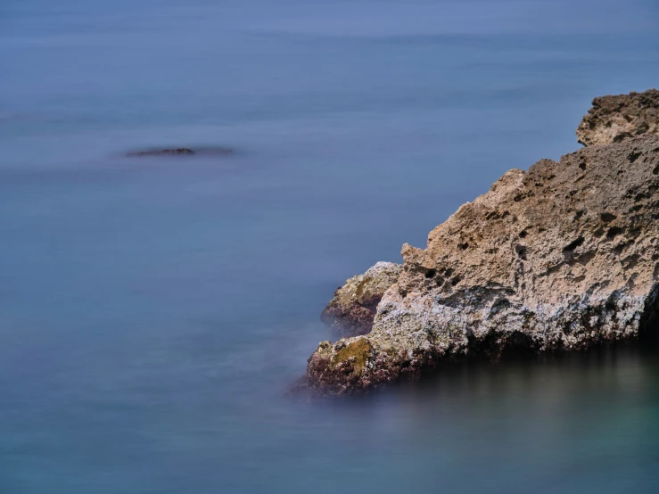 a large rock sticking out of the middle of some blue water