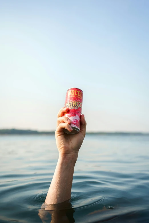 a hand holding a can of soda over the water